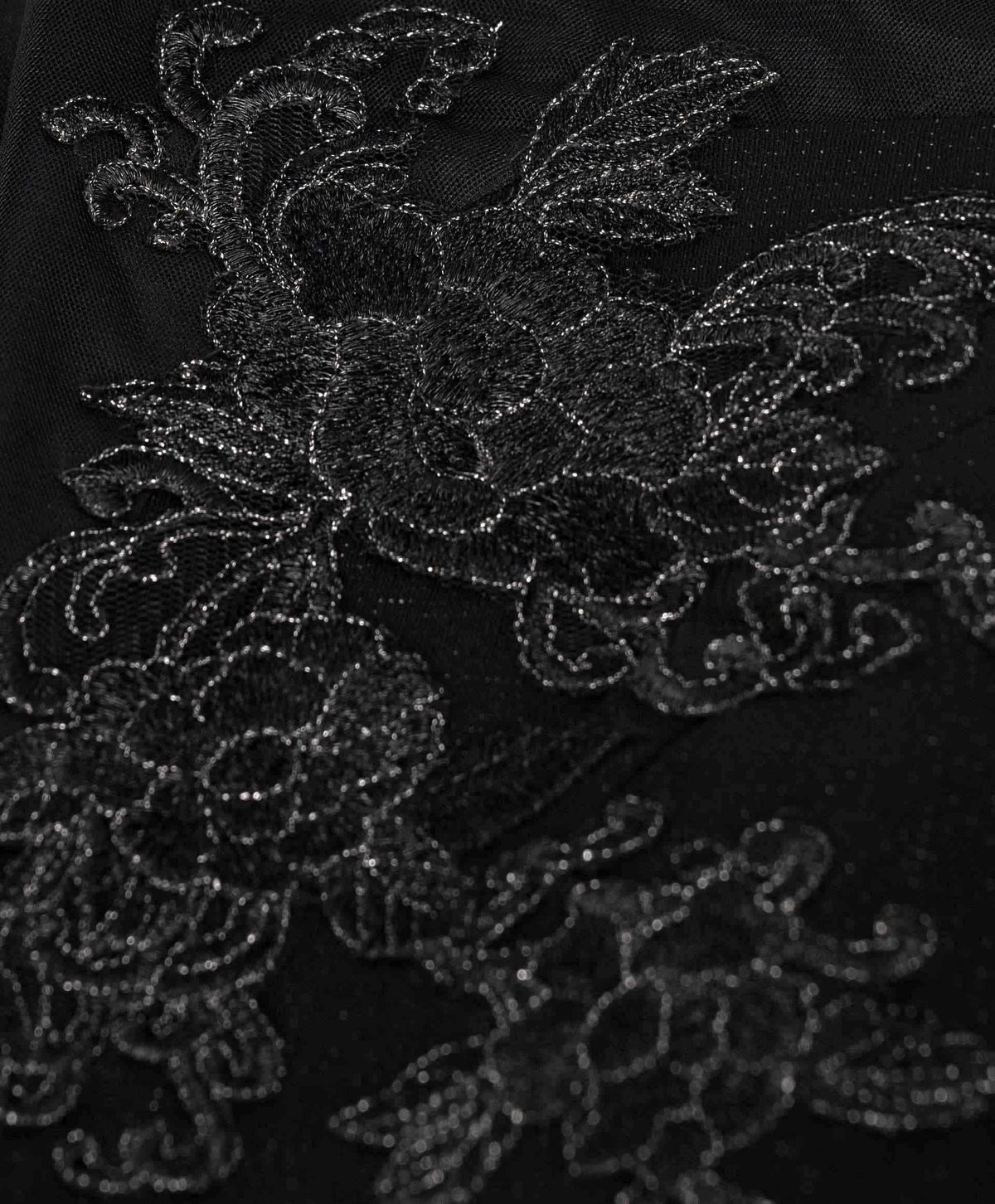 Dark floral outlines rise against the black surface, becoming visible through their texture and subtle glimmer.