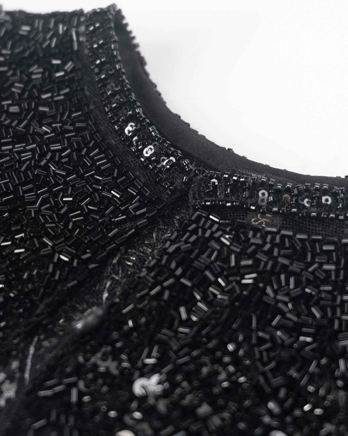Rows of small reflective beads follow the neckline and continue into the dark surface below.