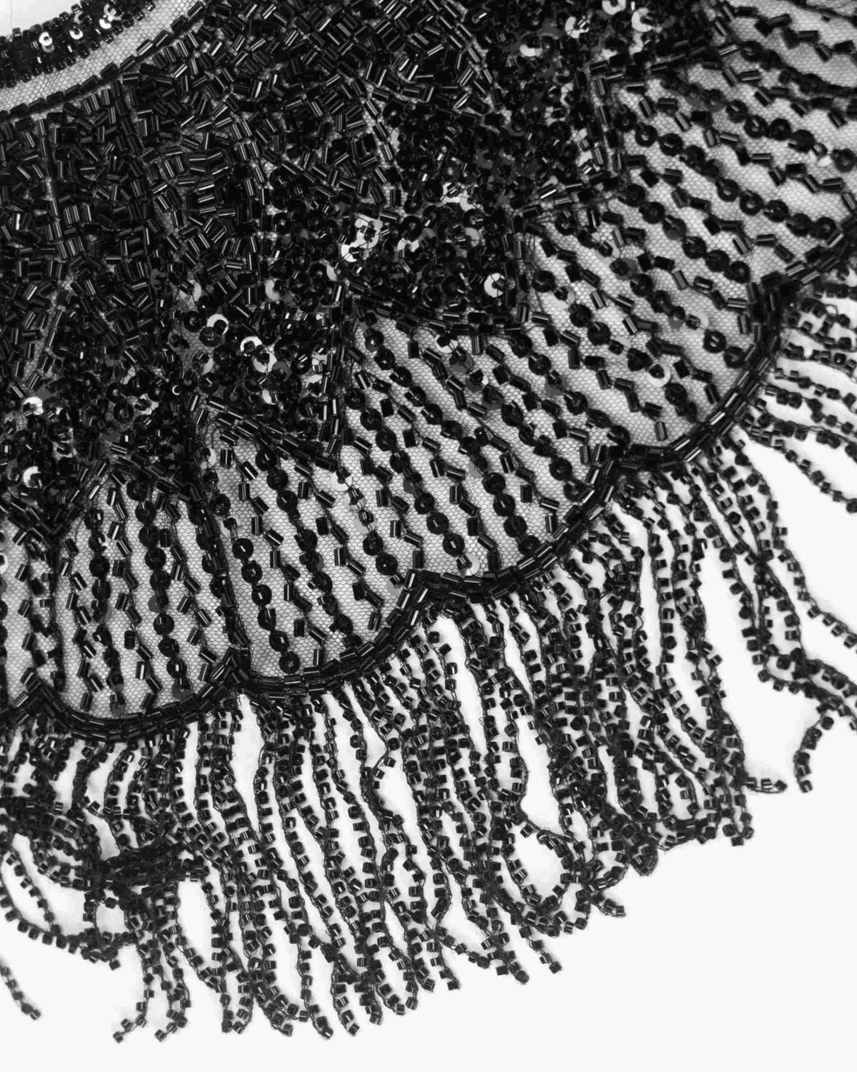 Fine dark strands descend from the shawl's lower edge, creating a repeated fringe beneath the more closely decorated surface.