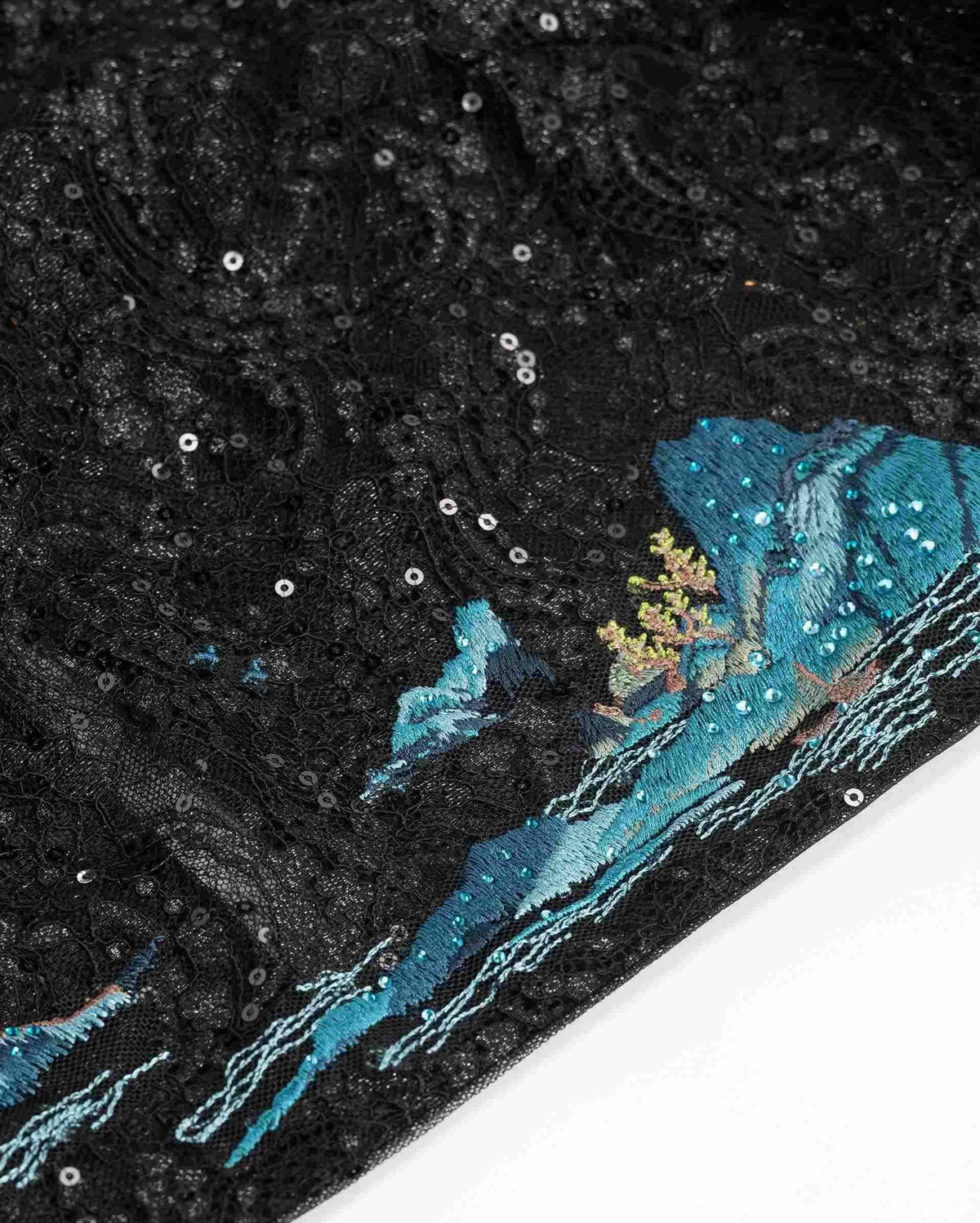 Blue landscape embroidery sits against the textured black lace, with fine reflective details nearby.